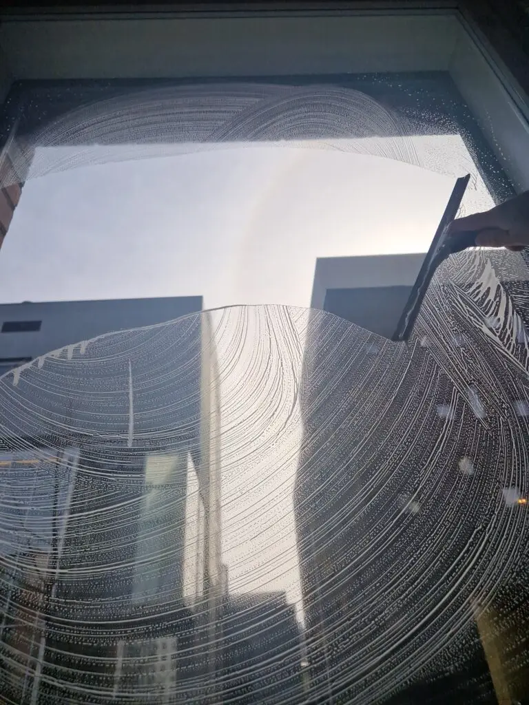 Ammattikäyttöön tarkoitettu ikkunankuivain kuivaamassa asunnon ikkunaa Helsingissä, taustalla taivas ja kerrostaloja